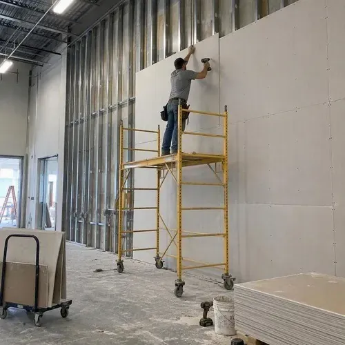 Worker on scaffold hanging tall commercial drywall on a commercial drywall project in Kingston, ON