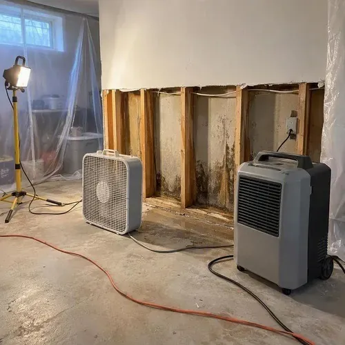 Fans drying an opened basement wall cavity during water damage drywall repair in Kingston, ON